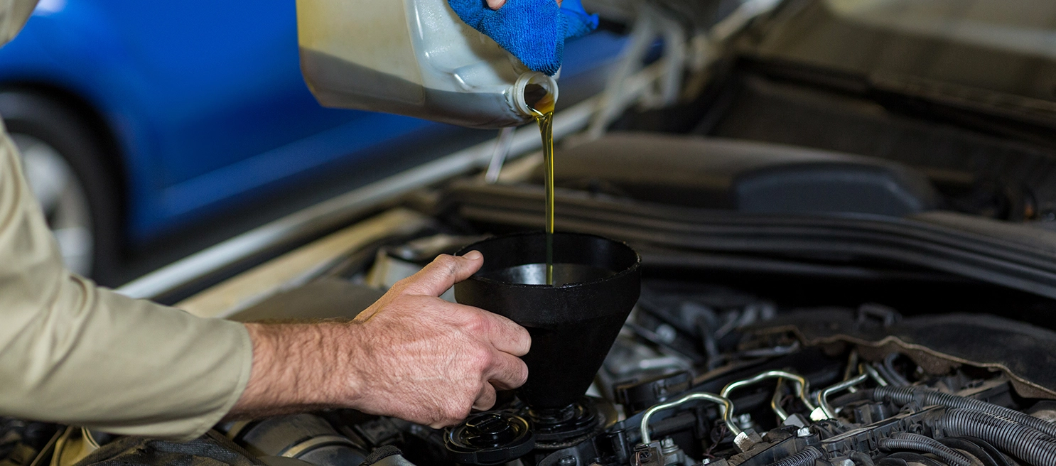 Foto de uma pessoa colocando óleo no motor de um carro com foco no óleo